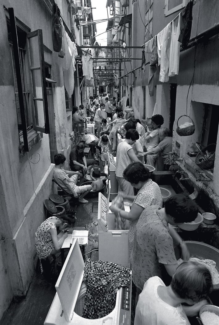 1990: A lane off Shanghai’s Guizhou Road is home to 72 households.  by Gong Jianhua  The term “72 households” has become synonymous with cramped housing in Shanghai. The classic comedy 72 Households set in Shanghai once caused a sensation. Over the past century, most Shanghai natives have suffered housing problems, so they still cite the term and the drama. In 2012, the photographer visited the alley again. It was still there but he could hardly recognize the people living there. He did meet the woman who is carrying a baby in the picture, who had matured into an old woman.